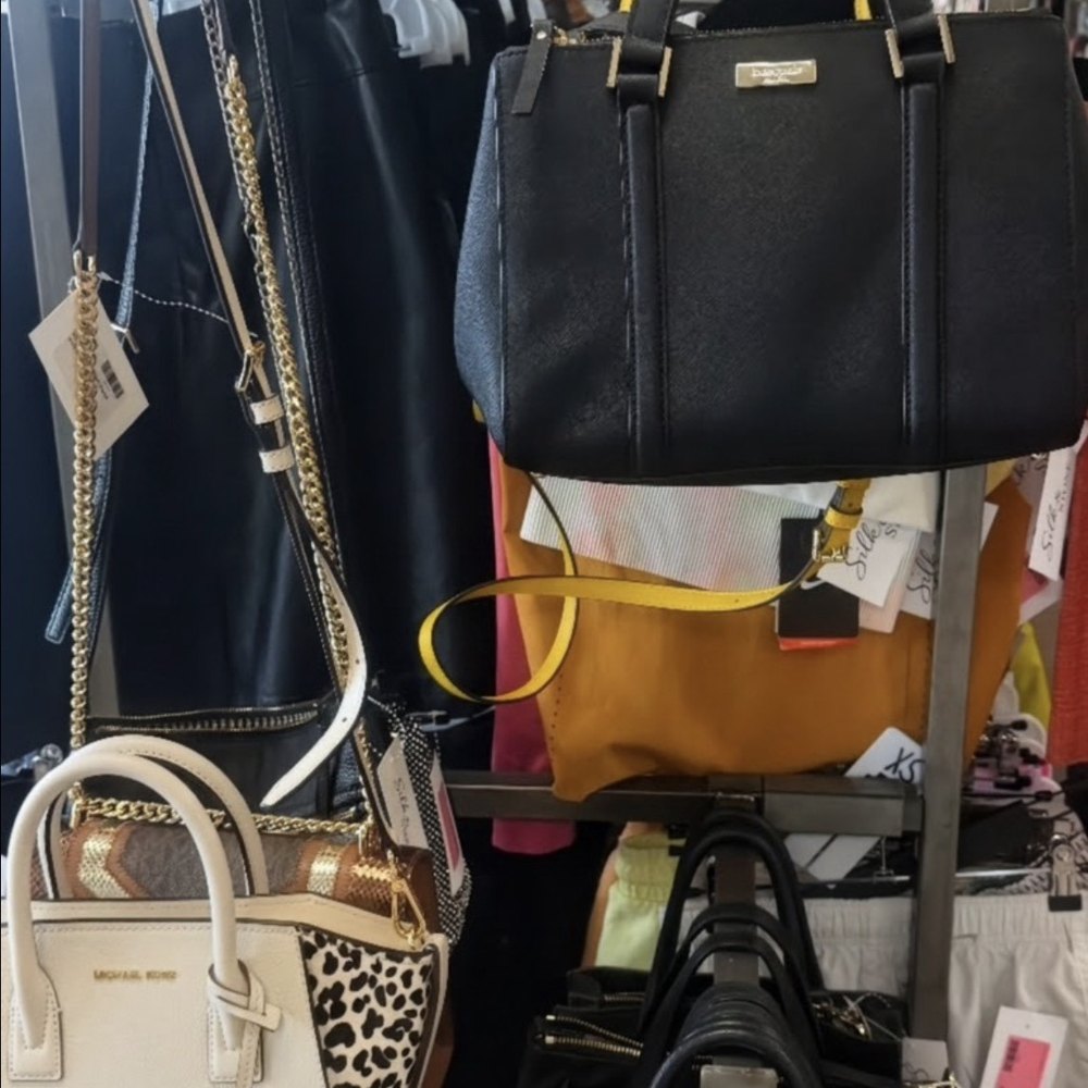 Handbags on the rack at Silk & Stone, including a black Kate Spade satchel and a cream Michael Kors bag, each tagged